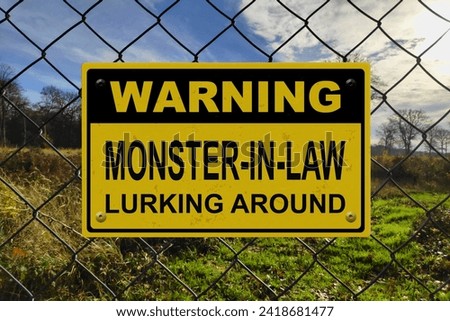 Black and yellow warning sign on a fence with the message "Warning - Monster-in-law lurking around".