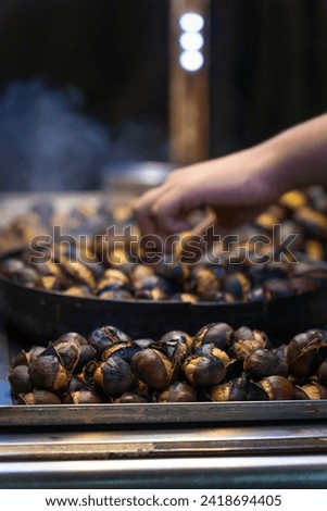 Close-up of the chestnut seller's hand roasting chestnuts outdoors on Istiklal Street. Vertical photo, focus on the foreground