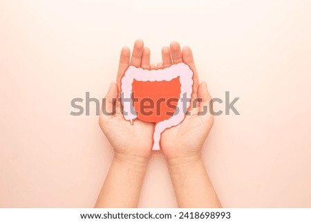 Hand holding large intestine organ made form paper on beige background. Concept of healthy bowel digestion, colon cancer screening, intestinal disease treatment or colorectal cancer awareness. Royalty-Free Stock Photo #2418698993