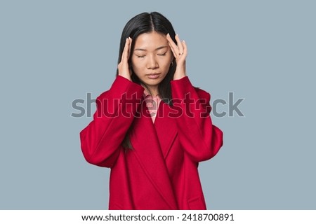 Young Chinese woman in studio setting touching temples and having headache.