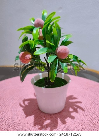 Plastic pink flowers in a white pot and their shadows on a pink knitted tablecloth in the shape of a circle
