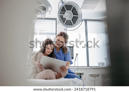 Supportive nurse watching cartoon on a tablet with children patient to her calm down. Concept of emotional support and friendliness for young kid patient. Royalty-Free Stock Photo #2418718791