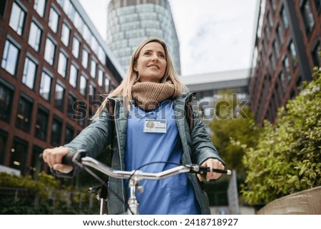 Beautiful nurse commuting through the city by bike. Doctor city leaving hospital by bike after long workday.