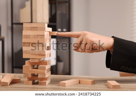 Playing Jenga. Man building tower with wooden blocks at table indoors, closeup Royalty-Free Stock Photo #2418734225