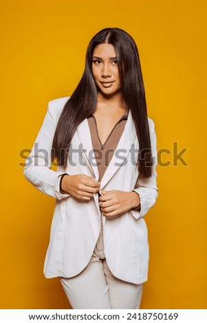 Portrait of a beautiful latin american businesswoman in suit posing at studio isolated over yellow background. Business concept. Vertical photo. Royalty-Free Stock Photo #2418750169