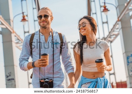 Photo of young happy couple at street walking drinking coffee and talking with each other, spending time together while traveling, sightseeing exploring the city