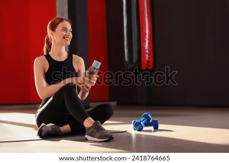 Athletic young woman with bottle of water on mat in gym, space for text