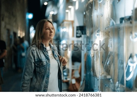 Woman looks at jewelry in store showcase at evening. Royalty-Free Stock Photo #2418766381