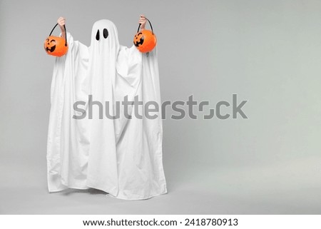 Child in white ghost costume holding pumpkin buckets on light grey background, space for text. Halloween celebration