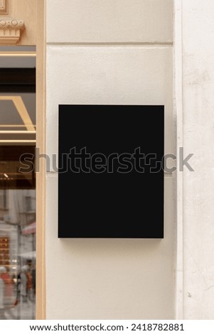 Wall-mounted black signboard on a textured wall, ideal for businesses to display their brand logo or promotional content. Black signage mockup.