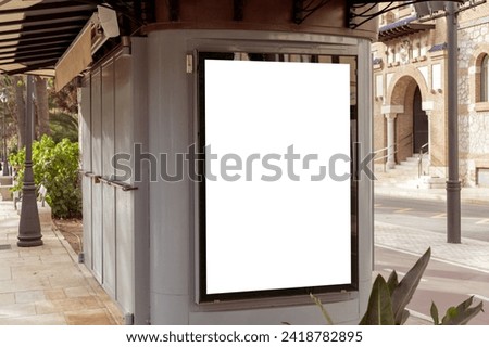 Empty outdoor advertisement space on a kiosk, nestled on a city street with tropical foliage, ideal for marketing and urban design. Copy space for your picture, text. Vertical billboard mock up.