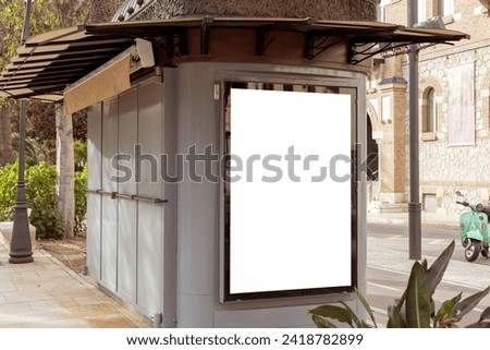 Empty outdoor advertisement space on a kiosk, nestled on a city street with tropical foliage, ideal for marketing and urban design. Copy space for your picture, text. Vertical billboard mock up.