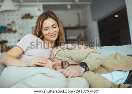 Happy married young couple hugging, sitting on cozy couch together, overjoyed laughing woman and man having fun, enjoying leisure time, relaxing on sofa in living room at home, good relationship