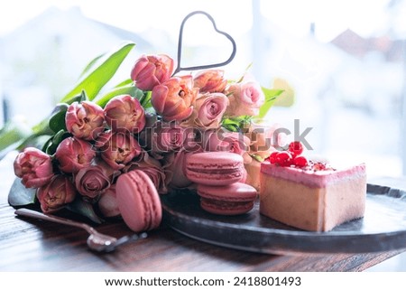 Beautiful bouquet of flowers with sweet delicacies. Heart shape, sweet pastries with pink roses and tulips on wooden table. Background for mother's day and wedding.
