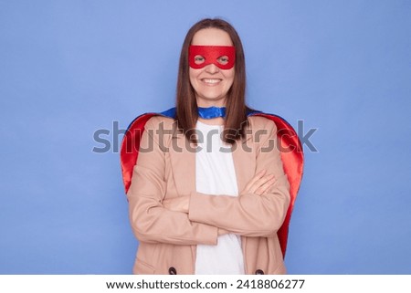 Confident delighted brown haired woman wearing superhero costume posing isolated over blue background looking at camera with toothy standing with crossed arms