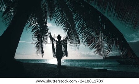 Elegant woman walk evening tropical beach under palm tree leaf. Slim joyful female silhouette raising hands, spin against sun down. Travel, relax, enjoy travel summer vacation. Blue filter back view