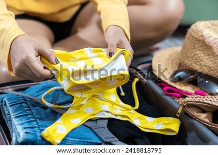A young woman preparing to pack her bikini into her travel bag for a weekend getaway