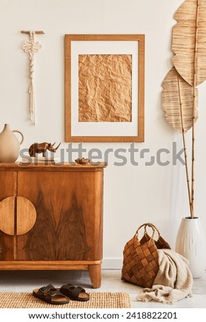 Minimalist composition of living room with brown mock up picture frame, carpet, macrame, dried tropical leaf, decoration and elegant personal accessories in stylish home decor. Template.