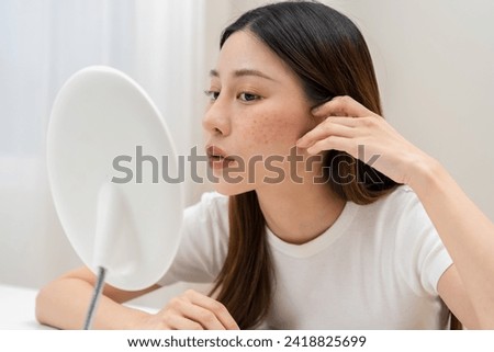 Dermatology, expression face worry asian young woman looking mirror hand touch face at dark spot of melasma, freckle from pigment melanin, allergy sun. Beauty care, skin problem treatment, acne care. Royalty-Free Stock Photo #2418825699