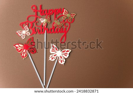 Butterfly paper letters wishing happy birthday on brown background. red letters and areas of white light hitting the background Add dimension to the image Suitable for wallpaper