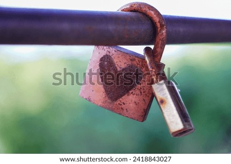 An old padlock with a painted heart hanging in the middle of a railing with many other padlocks. Concept Padlocks Love Forever. Valentine.