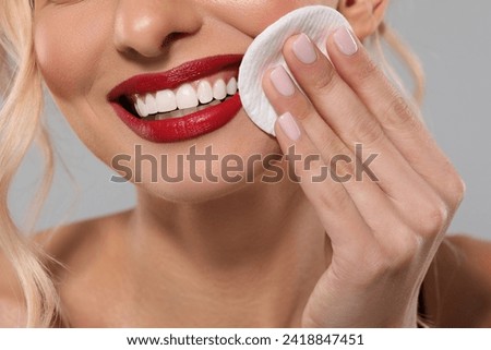 Smiling woman removing makeup with cotton pad on light grey background, closeup
