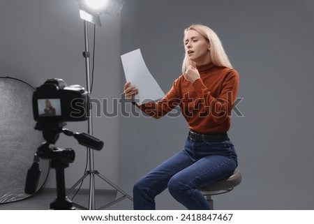 Casting call. Emotional woman with script sitting on chair and performing in front of camera in studio Royalty-Free Stock Photo #2418847467