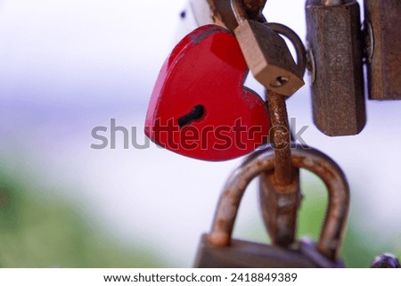 A red heart padlock hanging in the middle of a railing with many other padlocks. Concept Padlocks Love Forever. Happy Valentine Day.