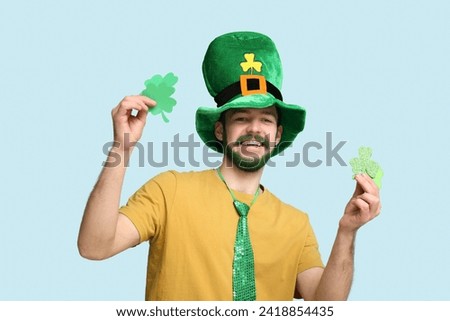 Young man in leprechaun hat with green beard holding clover on blue background. St. Patrick's Day celebration