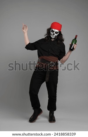 Man in scary pirate costume with skull makeup and bottle of rum on light grey background. Halloween celebration