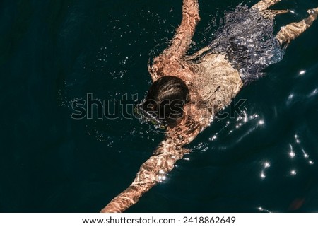 Top-down view of a young person swimming in the lake with goggles.