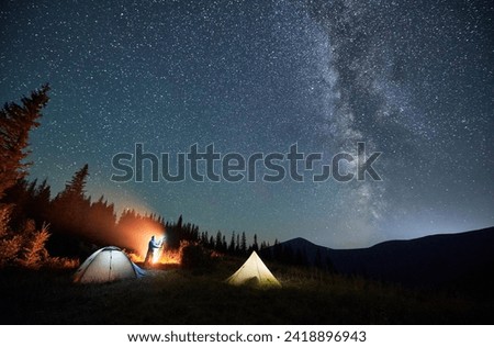 Male photographer taking pictures of Milky way. Man doing photo shoot of starry sky next to his camping. Starry night in mountains.