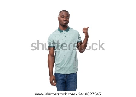 young slender American man dressed in a T-shirt and jeans points his hand to the side Royalty-Free Stock Photo #2418897345