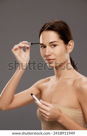 Tutorial on makeup techniques for enhancing natural beauty. Woman holding brow fixing gel against studio background against background. Concept of natural beauty, cosmetology and cosmetics, skin care