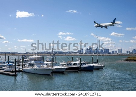 A plane soars over a marina, embracing the skies above a sea of anchored boats. Royalty-Free Stock Photo #2418912711