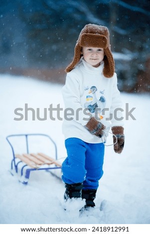 Portrait of a 4-year-old boy who is driving a sled to go down a hill and have a laugh in winter