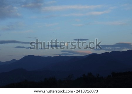 white full moon rising behind a mountain ridge illuminating misty clouds creating a mystical atmosphere. glowing round moon rising into the night sky with layers of hills. luna above peak. night scene