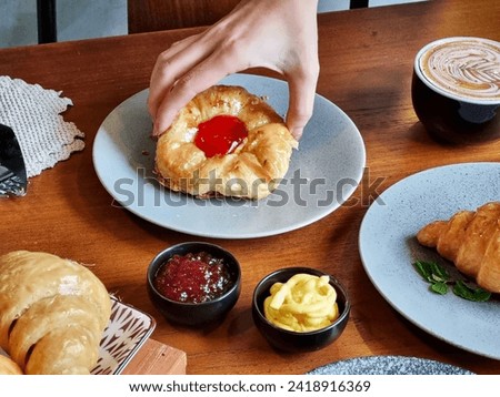 Several freshly baked croissants on a ceramic plate, next to a cup of coffee, a small jar of cream and jam. This image is suitable for cafe menus, food blogs, lifestyle magazines and culinary sites.