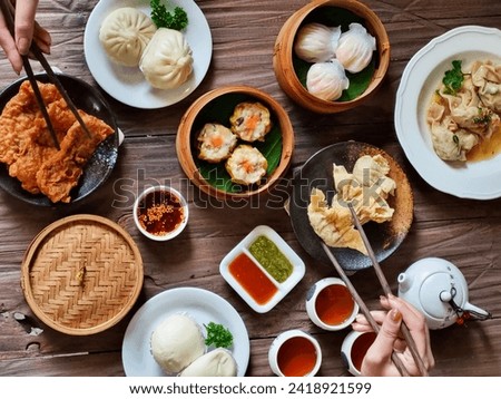 Image of various Chinese dim sum in a bamboo steamer, equipped with chopsticks and tea, on a wooden table. Perfect for illustrating Asian cooking articles, restaurant menus and food blog content.