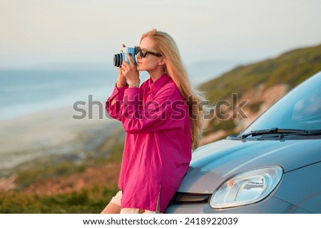 Blond woman takes a photo overlooking the sea at sunset.Stylish retro camera.