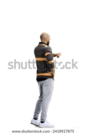 A man, on a white background, in full height, looks at his watch