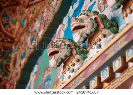 Snow lions with turquoise manes bas reliefs on wall above entrance to Buddhist temple, decorative and religious decoration of ancient temple facade, snow lions mythological celestial animal of Tibet Royalty-Free Stock Photo #2418941687
