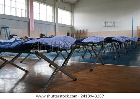 Cots with sleeping bags are placed in the school gym during an emergency Royalty-Free Stock Photo #2418943239
