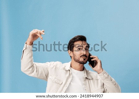 Portrait of a brunette man animation and joy talking on the phone hand and fist up from joy victory and happiness smile with teeth, on a blue background in a white T-shirt and jeans, copy space
