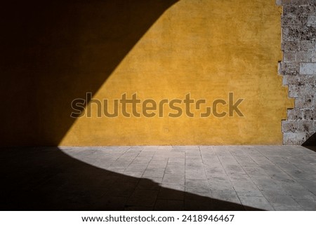 A contrasting yellow textured background with shadow and stone cast in the sunlight. backdrop that can be used in photo manipulations for fashion and product placement or web design. room for text.