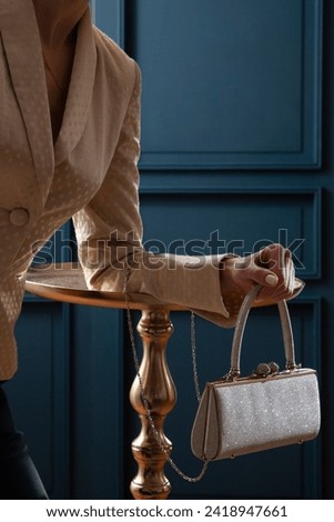 Shiny sparkling silvery clutch woman hand bag with model in yellow dotted jacket on a blue background with party feeling. Fashion studio shot  Royalty-Free Stock Photo #2418947661
