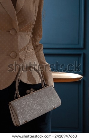 Shiny sparkling silvery clutch woman hand bag with model in yellow dotted jacket on a blue background with party feeling. Fashion studio shot  Royalty-Free Stock Photo #2418947663