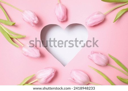 Heart surrounded with fresh tulips on pastel pink background