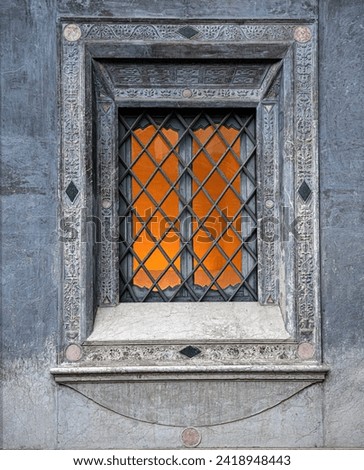 Old Italian window with grids bathed in a warm, orange glow. Orange light behinde the grids.