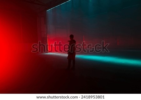 A lone figure stands taking a picture in a backlit warehouse environment art installation that could depict a club type environment